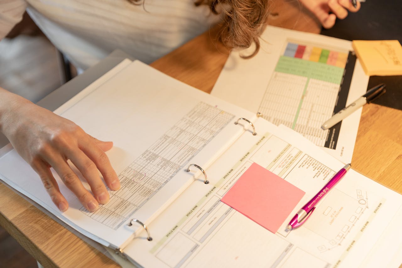 Close-up of an employee sorting documents with sticky notes and pens on a wooden desk.